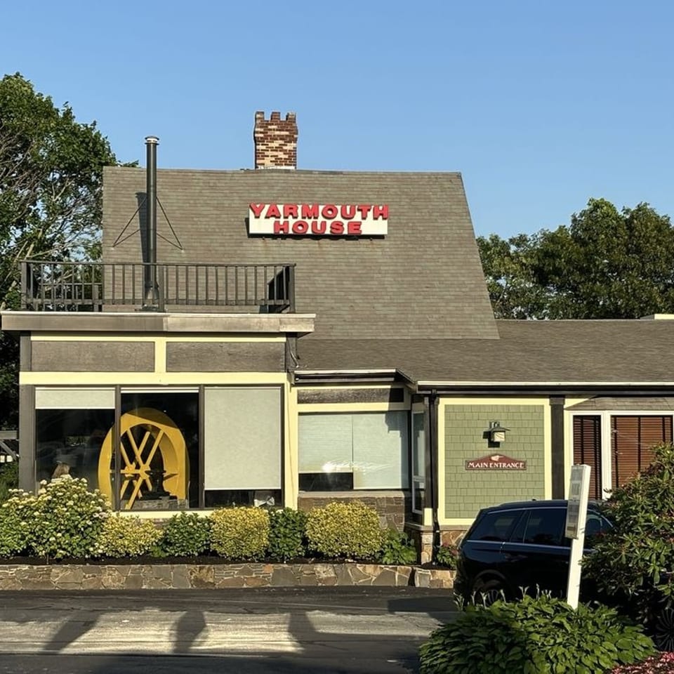 Yarmouth House restaurant exterior with a shingled roof, brick chimney, terrace, landscaped gardens, and entrance sign.