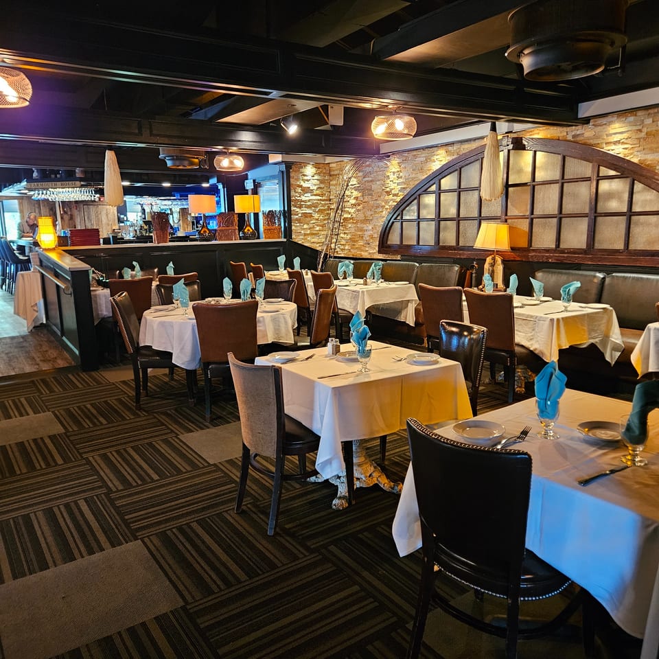 Elegant restaurant dining room with white tablecloths, turquoise napkins, leather chairs, warm lighting, stone walls, and a bar.